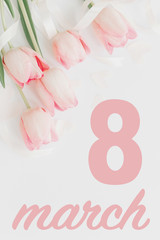 8 march. Happy womens day greeting card. 8 march text on pink tulips with ribbon on white background, vertical flat lay. Stylish tender image. Handwritten lettering. International women day