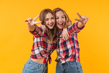 Image of two young beautiful girls smiling and gesturing peace sign