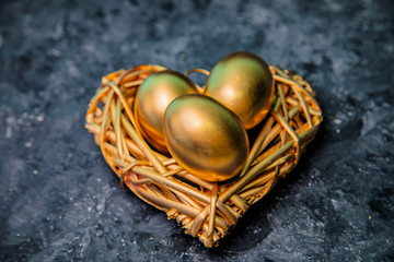 On a black background lie golden eggs and a golden heart. 