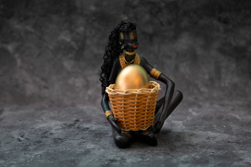 African AmericanFigurine of an African American with a basket with a golden egg on a black...