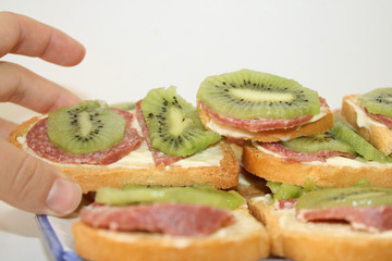 Sandwich with salami and kiwi, hand takes