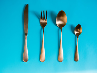 set of tableware. Knife fork spoon made of yellow metal imitating gold on a blue background