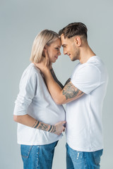 side view of young tattooed pregnant woman with boyfriend isolated on grey