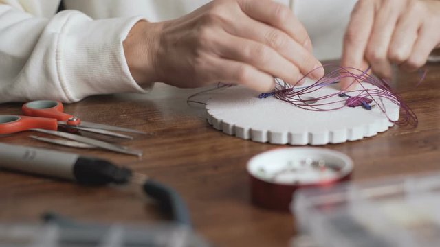 Lifestyle concept, work from home to reinvent your life: close-up of woman hands making macrame knotted jewelry with stone beads and tools on wooden table