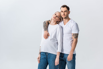 Fototapeta premium young tattooed pregnant woman embracing with husband isolated on grey