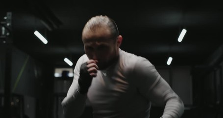 Strong adult man doing shadow boxing and performing various punches during workout in dark gym. - Powered by Adobe