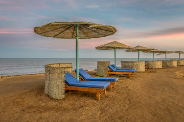 loungers and shelters in a row at the sunset on a tropical beach