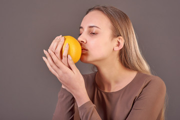 A young beautiful girl holds an orange in her hands and sniffs its smell.