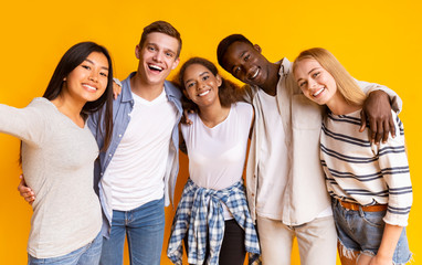 Friendly international group of teenagers taking selfie over yellow background