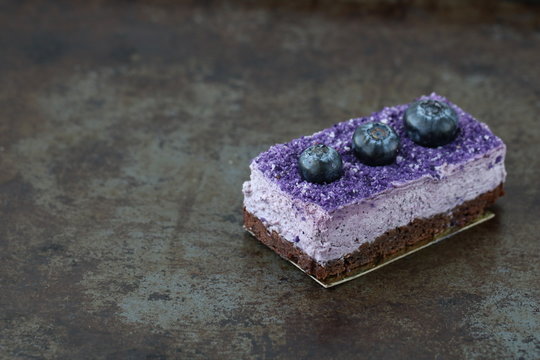 Tasty purple blueberry mousse cake with blueberry on rust background, horizontal, side view, copy space, selective focus