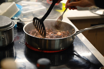 Hand using kitchen flipper frying sliced beef in pan