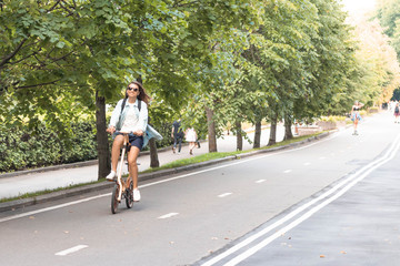 Fototapeta na wymiar Happy white woman in casual wear rides a folding bike in the park on a warm day against a background of bright foliage. Summer or spring life style.