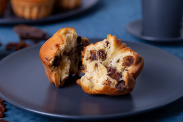 Muffins with chocolate and raisins. Homemade baking. In the background is a plate with muffins and a cup of coffee. Blue background. Close-up.