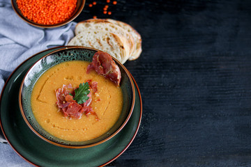 Lentil soup on a wooden background. Served with sliced bacon and herbs. Nearby are pieces of ciabatta. Raw groats in the background.