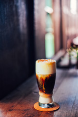 Iced coffee cappuccino   with cream poured over in a tall glass on wooden table