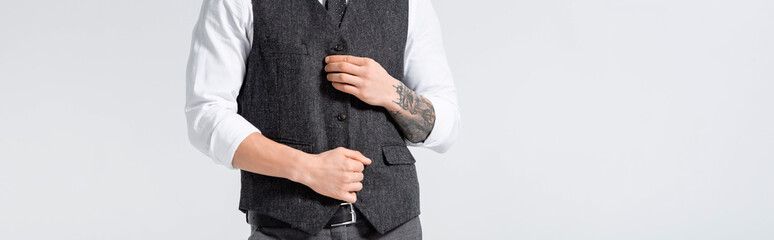 cropped view of tattooed elegant bridegroom buttoning waistcoat isolated on white, panoramic shot