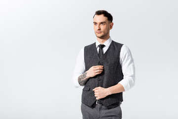 handsome tattooed elegant bridegroom buttoning waistcoat isolated on white
