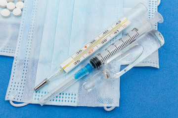 medical protective masks with thermometer, syringe, ampoule, medicine bottle, pills on a blue background.