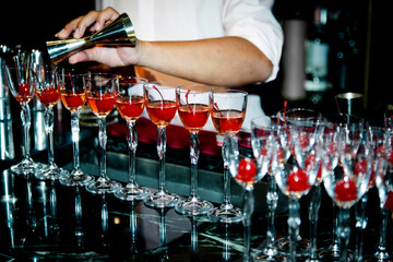 Bartender makes red cocktail in a bar with fresh cherry.