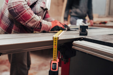 Worker in a carpentry shop measures plywood for cutting