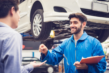 Obraz premium Mechanic holding clipboard giving the key back to car owner in the workshop garage. Car auto services concepts