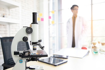 Close-up view of the microscope is placed on the table in the laboratory with the background blurred while the doctor is standing waiting for the patient. Research and experimentation concepts
