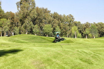 The jet of water watering the lawn for a game of Golf. Golf course with hills and plains, trees and...