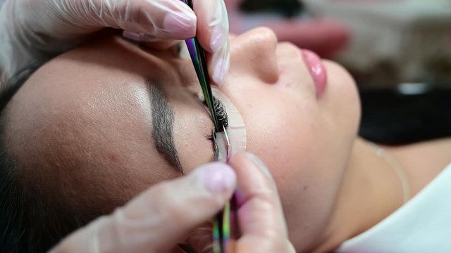 Close-up of a beautiful asian woman on eyelash extension procedure. Double volume false eyelashes. Lashmaker at work.