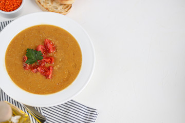 Vegetable soup with lentils on a white background. Served with chopped cherry tomatoes and herbs. Nearby are pieces of ciabatta. Raw groats in the background. Vegetarian dish.