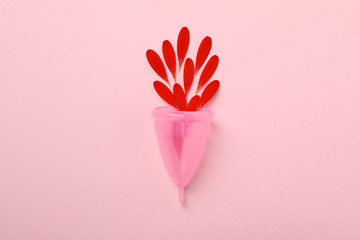Menstrual cup and gerbera petals on pink background, space for text