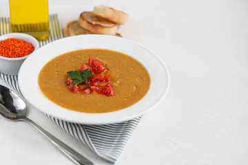 Vegetable soup with lentils on a white background. Served with chopped cherry tomatoes and herbs. Nearby are pieces of ciabatta. Raw groats in the background. Vegetarian dish.