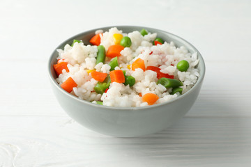 Bowl of delicious rice with vegetables on wooden background, close up