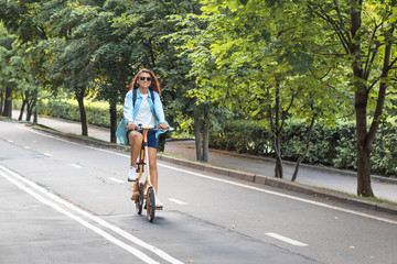 Happy white woman in casual wear rides a folding bike in the park on a warm day against a background of bright foliage. Summer or spring life style.