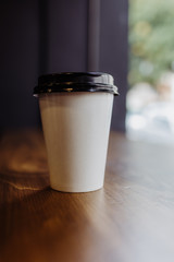 A white to-go coffee cup on a table near a window