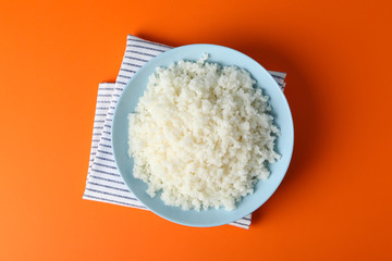 Bowl with boiled rice on orange background, top view