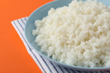 Bowl with boiled rice on orange background, close up