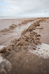 Tyre tracks going off in the distance on a golden sandy beach on an overcast day. moving forward progression and driving off road on the beach