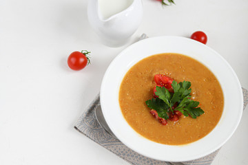Vegetable soup with lentils on a white background. Served with chopped cherry tomatoes and herbs. Nearby are pieces of ciabatta. Raw groats in the background. Vegetarian dish.