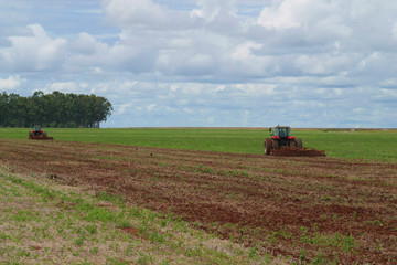 Fototapeta premium Trator no campo plantando soja, 2 tratores, solo preparado, céu com nuvens anunciando chuva