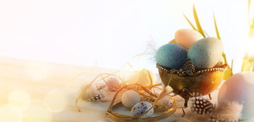 Art Easter eggs basket and bird feather on sunny wooden background; Holiday Easter banner or greeting card background