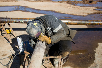 Welder in protective clothing for welding. Pipe preparation for a drilling rig. At the construction site.