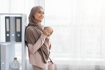 Cheerful Arabic Businesswoman With Cup Of Coffee Near Window In Office