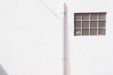 white wall with pipe and background window in daylight