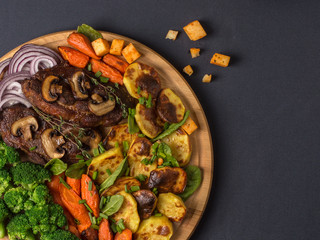 fried steaks with potatoes, carrots and broccoli on a wooden board.