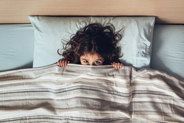 little girl covering her face with the bedspread