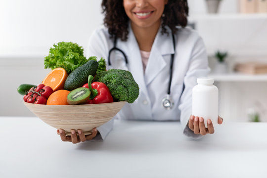 Nutritionist holding bowl with fruits, vegetables and bottle of pills