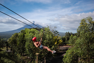 Fototapeta na wymiar Young girl zip lining with a volcano in the background