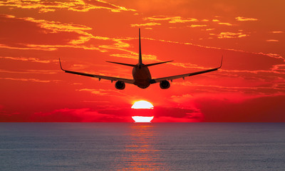 Naklejka na ściany i meble Airplane flying above tropical sea at sunset