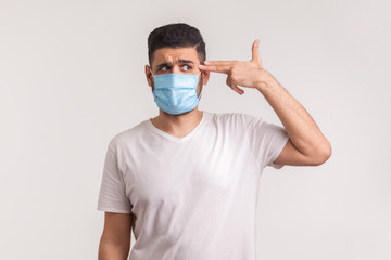 Coronavirus mortality. Desperate man in hygienic mask pointing finger gun to head, afraid of infection, respiratory illnesses such as flu, 2019-nCoV, ebola. studio shot isolated on white background