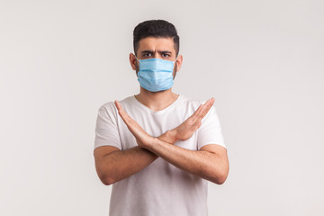 Man in protective hygienic mask standing with crossed arms, gesturing stop, warning of coronavirus epidemic, infection, respiratory diseases such as flu, 2019-nCoV, ebola. indoor studio shot, isolated